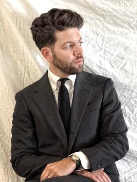 A man wearing a charcoal Rochester Tailored Clothing suit jacket with a white shirt and knit tie