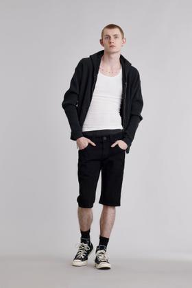 A man wearing black Rock Revival denim shorts with a black zip hoodie and white tank top