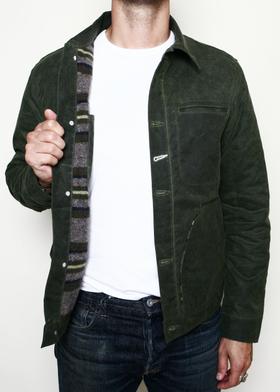 A man wearing a dark green waxed-canvas Rogue Territory jacket with striped blanket lining over a white tee and jeans