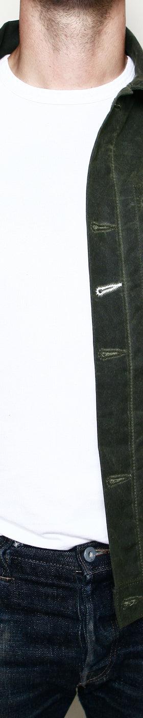 A man wearing a dark green waxed-canvas Rogue Territory jacket with striped blanket lining over a white tee and jeans