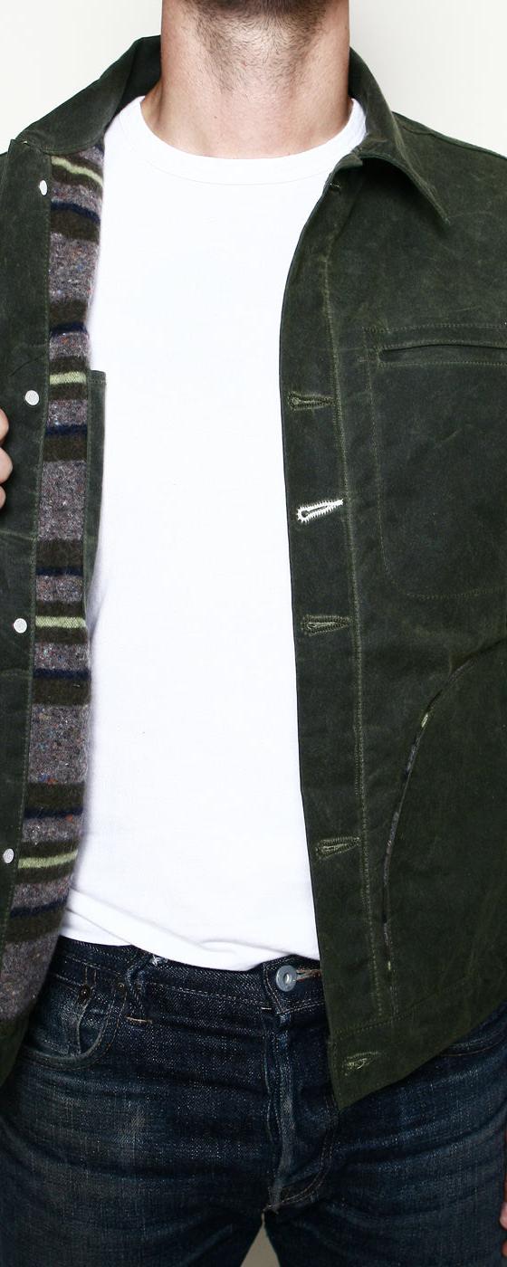 A man wearing a dark green waxed-canvas Rogue Territory jacket with striped blanket lining over a white tee and jeans