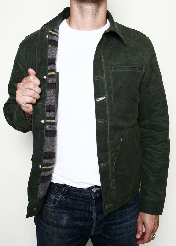 A man wearing a dark green waxed-canvas Rogue Territory jacket with striped blanket lining over a white tee and jeans