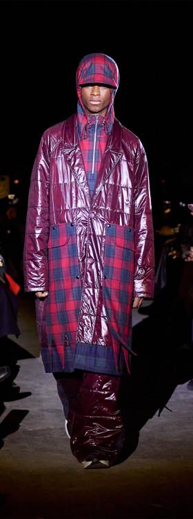 A man wearing a glossy burgundy Rolf Ekroth puffer coat over a red tartan check ensemble with a matching flat cap