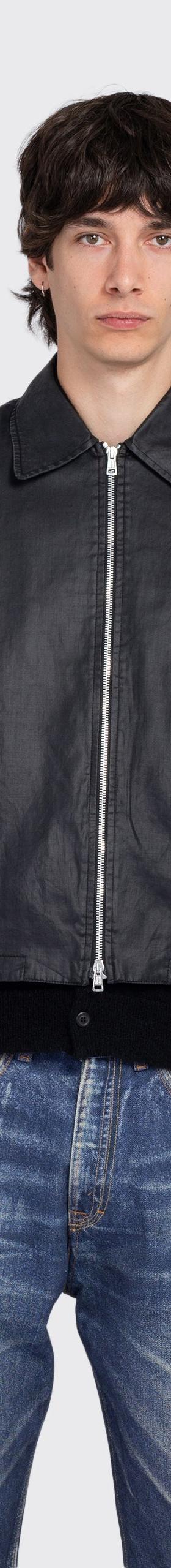 A man wearing a black coated denim zip jacket with faded blue jeans