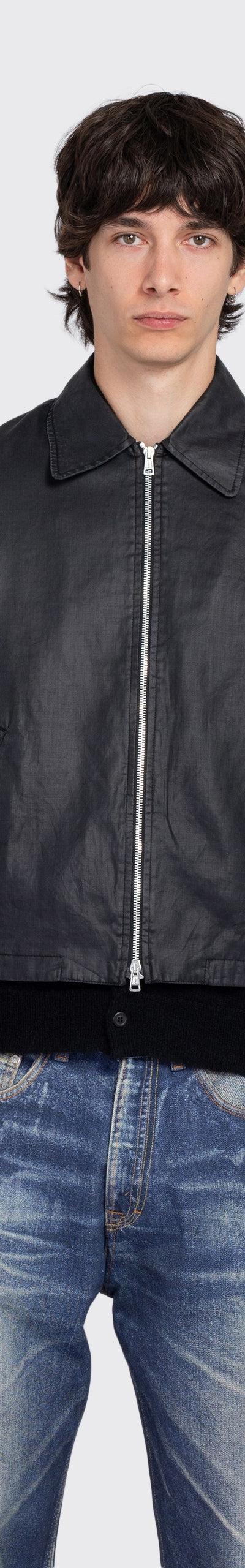A man wearing a black coated denim zip jacket with faded blue jeans