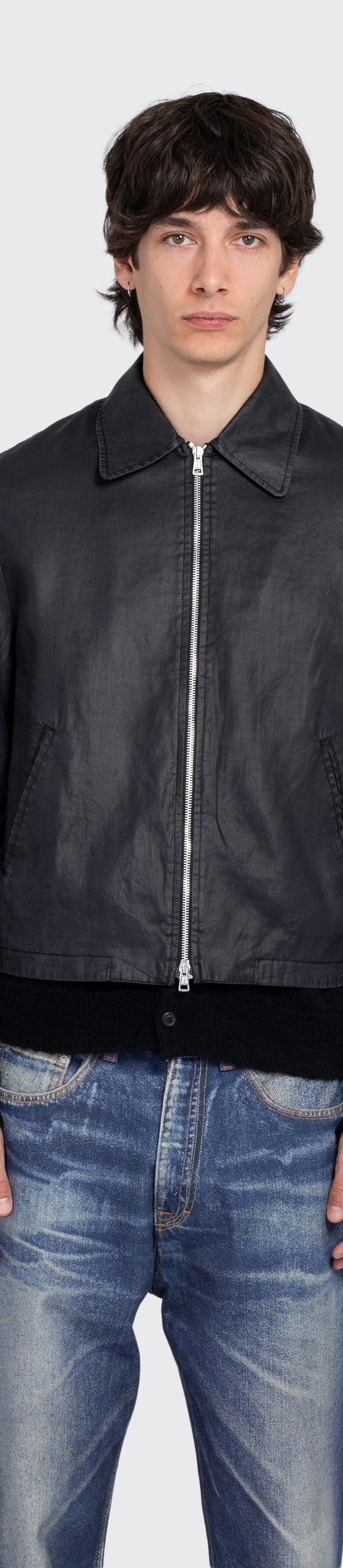 A man wearing a black coated denim zip jacket with faded blue jeans
