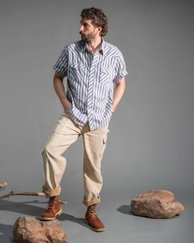 A man wearing a blue striped short-sleeve shirt, cream cargo trousers and tan leather Rose Anvil boots