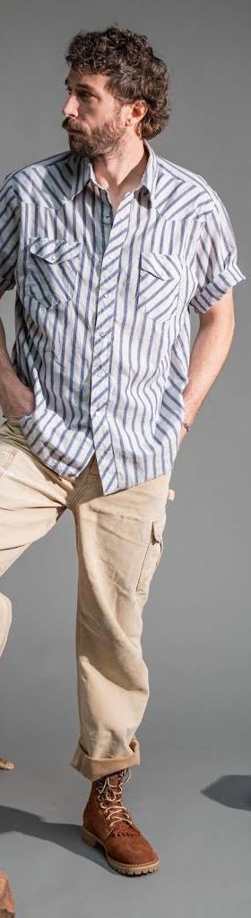 A man wearing a blue striped short-sleeve shirt, cream cargo trousers and tan leather Rose Anvil boots