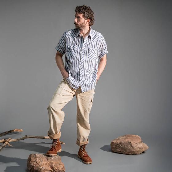 A man wearing a blue striped short-sleeve shirt, cream cargo trousers and tan leather Rose Anvil boots
