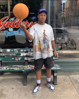 A man wearing a Round Two vintage graphic tee, black shorts and Jordan 1 sneakers outside the Round Two store