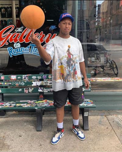 A man wearing a Round Two vintage graphic tee, black shorts and Jordan 1 sneakers outside the Round Two store