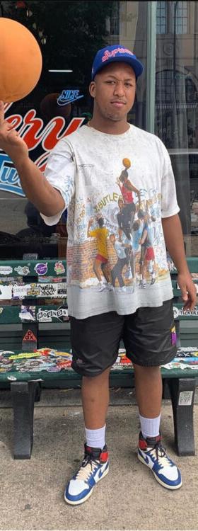 A man wearing a Round Two vintage graphic tee, black shorts and Jordan 1 sneakers outside the Round Two store
