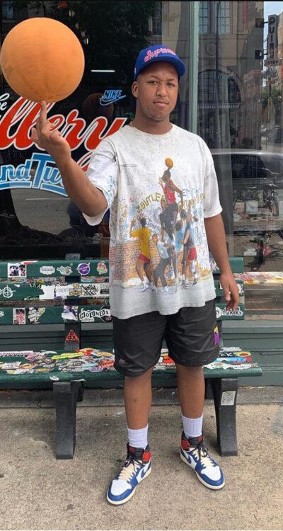 A man wearing a Round Two vintage graphic tee, black shorts and Jordan 1 sneakers outside the Round Two store