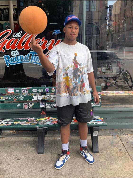 A man wearing a Round Two vintage graphic tee, black shorts and Jordan 1 sneakers outside the Round Two store