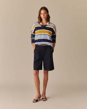 A woman wearing a navy, yellow and pale blue striped Rowing Blazers rugby-collar sweater with navy pleated shorts