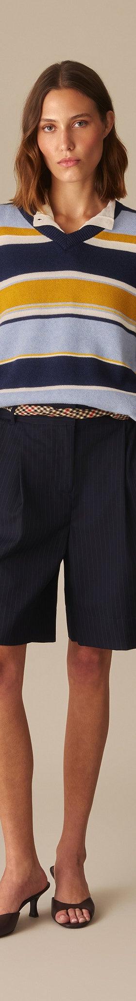 A woman wearing a navy, yellow and pale blue striped Rowing Blazers rugby-collar sweater with navy pleated shorts