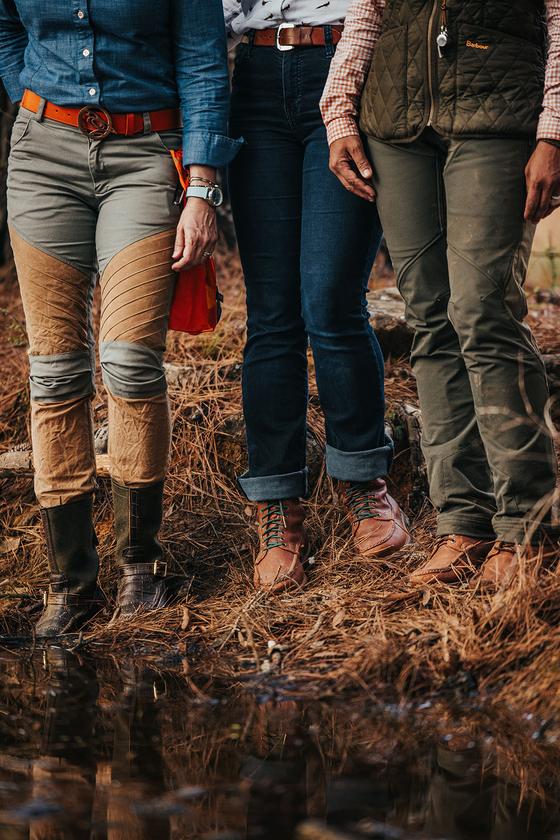 Three people standing at a marshy water's edge wearing Russell Moccasin lace-up boots and knee-high field boots