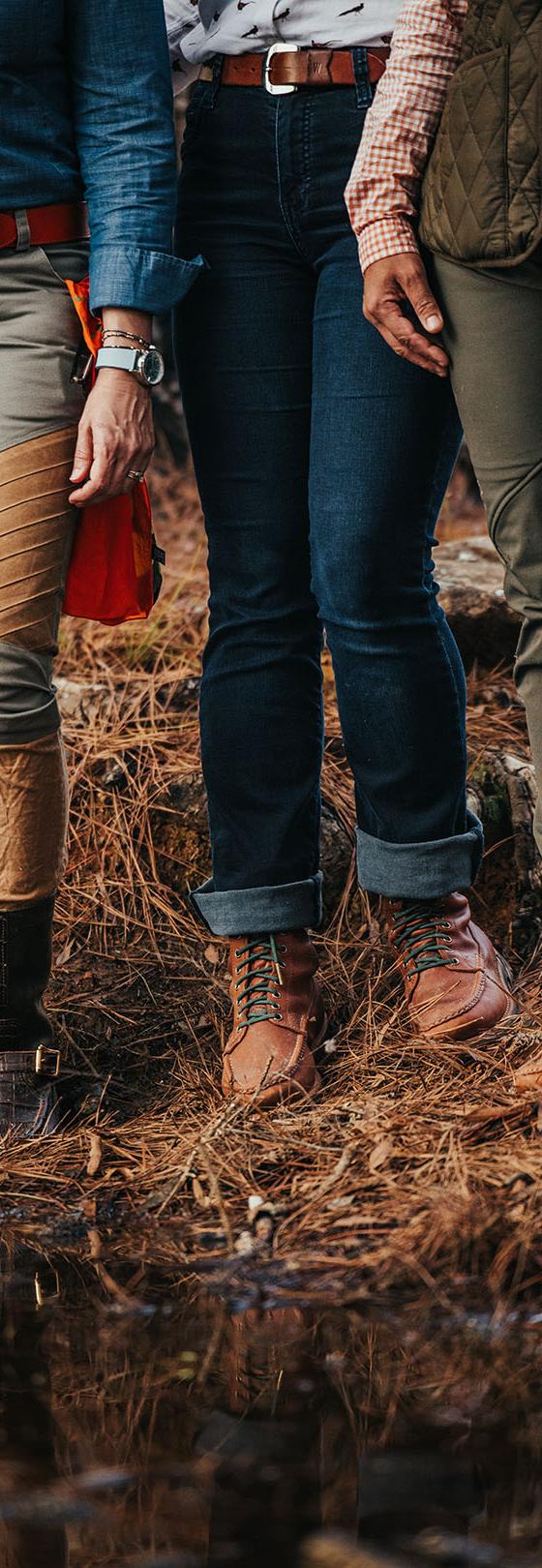 Three people standing at a marshy water's edge wearing Russell Moccasin lace-up boots and knee-high field boots