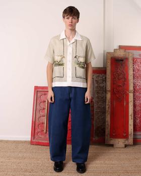 A man wearing an S.S.DALEY linen camp-collar shirt with pastoral sheep print and wide indigo jeans