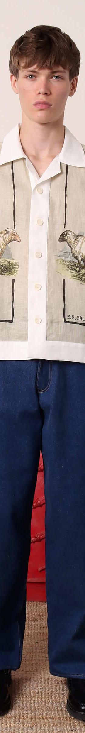 A man wearing an S.S.DALEY linen camp-collar shirt with pastoral sheep print and wide indigo jeans