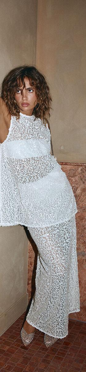 A woman wearing a sheer white lace Sabo top and matching maxi skirt