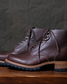 A pair of Saddleback Leather Co. Huntsman boots in dark coffee brown leather with black lug soles on a wooden table