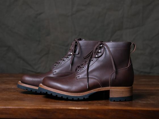 A pair of Saddleback Leather Co. Huntsman boots in dark coffee brown leather with black lug soles on a wooden table