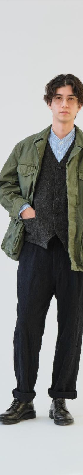 A man wearing an olive SAGE DE CRET field jacket over a knitted vest and black trousers