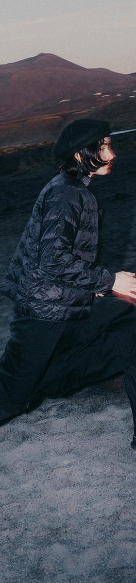 A man in a black quilted jacket, wide black trousers and Salomon Advanced trail sneakers striding across volcanic terrain at dusk