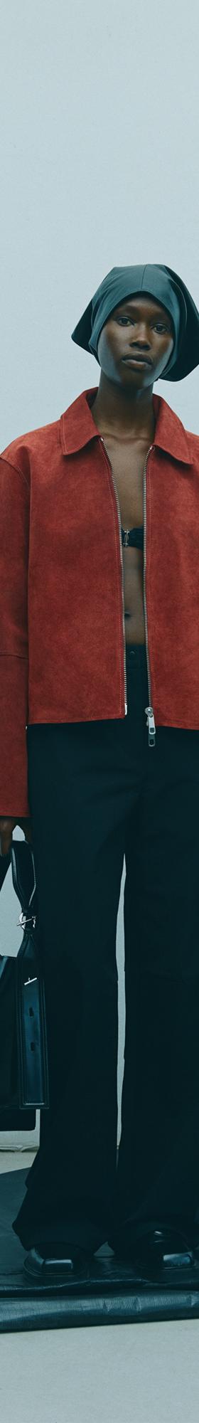 A woman wearing a rust suede Samsøe Samsøe jacket with black wide-leg trousers and a black leather bag
