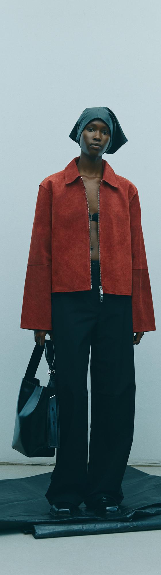 A woman wearing a rust suede Samsøe Samsøe jacket with black wide-leg trousers and a black leather bag
