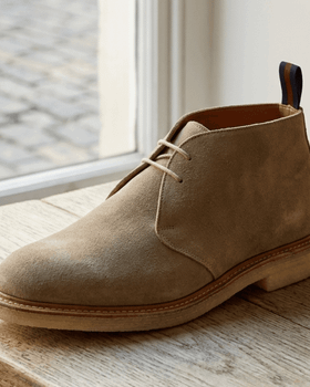 A sand suede Sanders chukka boot with crepe sole on a wooden windowsill