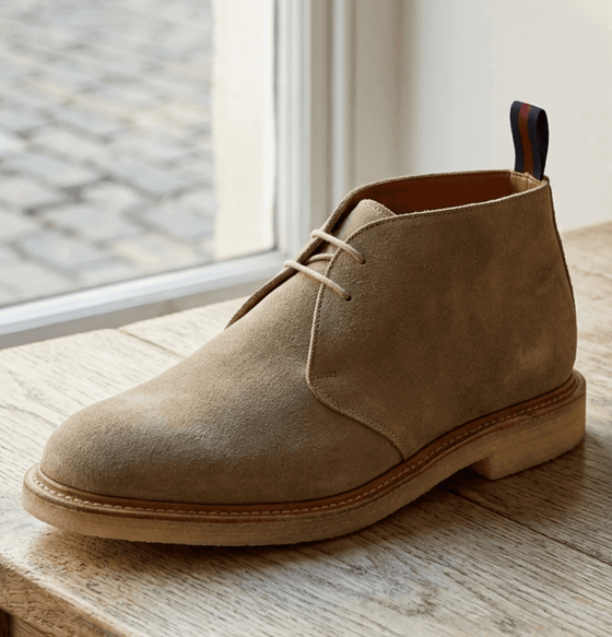 A sand suede Sanders chukka boot with crepe sole on a wooden windowsill