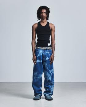 A man wearing a black Saul Nash ribbed tank top with wide-leg printed blue jeans