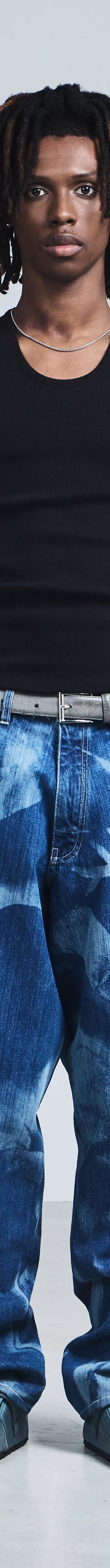 A man wearing a black Saul Nash ribbed tank top with wide-leg printed blue jeans