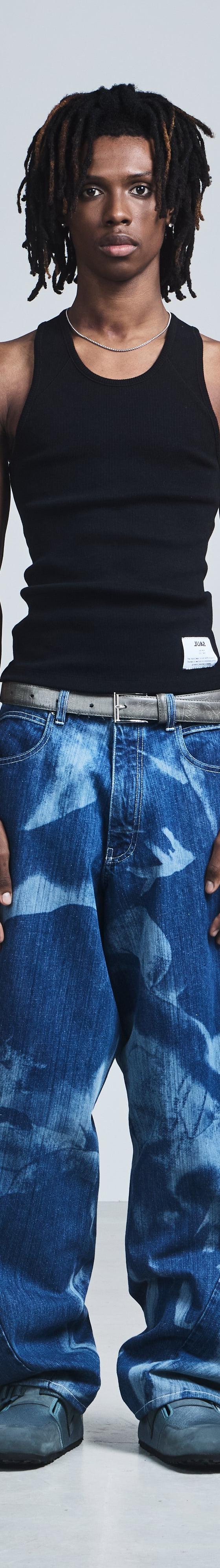 A man wearing a black Saul Nash ribbed tank top with wide-leg printed blue jeans