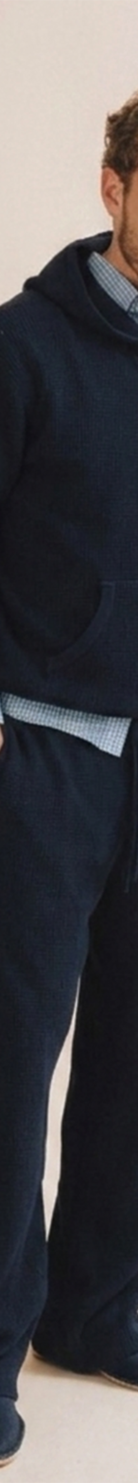 A man wearing a navy Save Khaki United hooded sweatshirt and matching sweatpants over a checked shirt