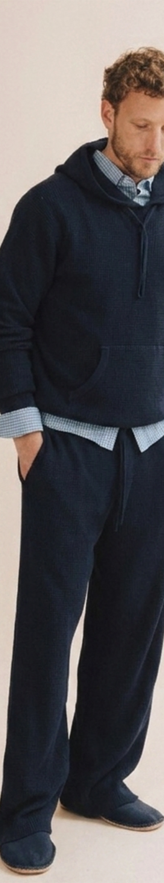 A man wearing a navy Save Khaki United hooded sweatshirt and matching sweatpants over a checked shirt