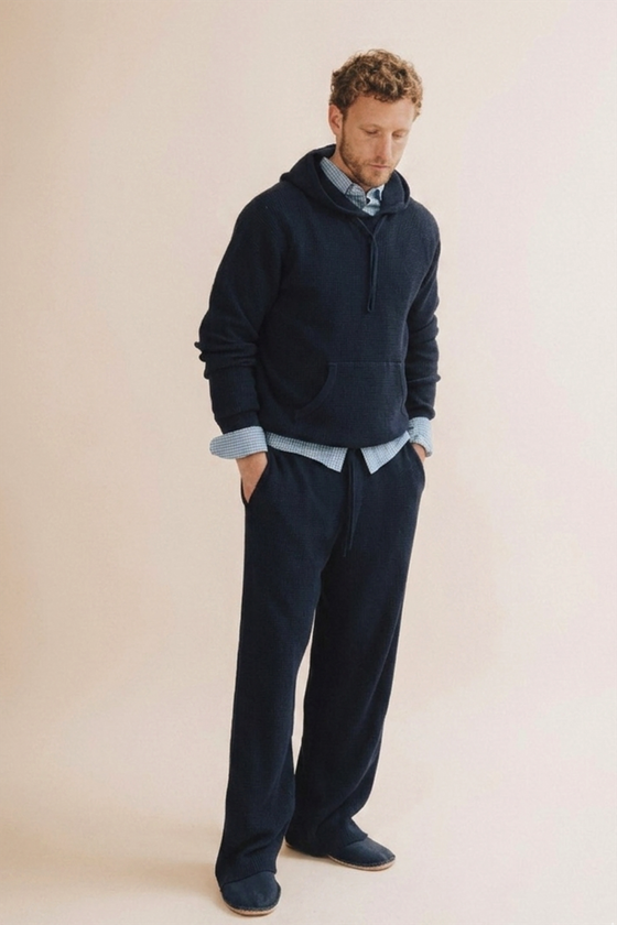 A man wearing a navy Save Khaki United hooded sweatshirt and matching sweatpants over a checked shirt