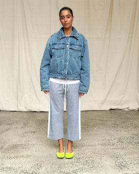 A woman wearing an oversized Scarlet and Sam denim jacket with grey side-stripe track pants and lime ballet flats