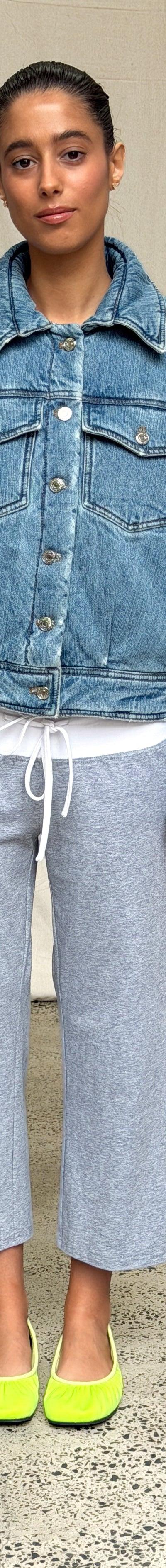 A woman wearing an oversized Scarlet and Sam denim jacket with grey side-stripe track pants and lime ballet flats