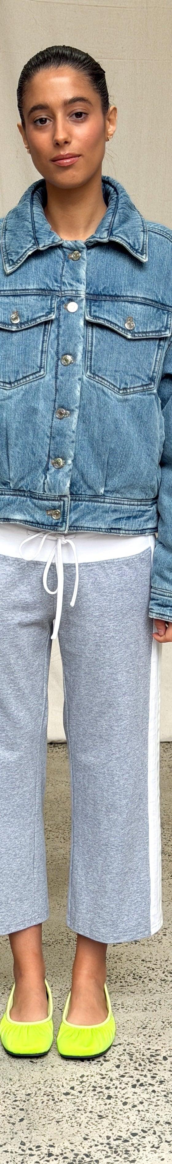 A woman wearing an oversized Scarlet and Sam denim jacket with grey side-stripe track pants and lime ballet flats