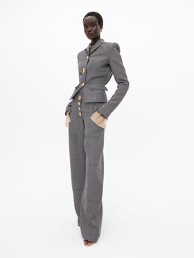 A woman wearing a grey Schiaparelli tailored jacket and wide-leg trousers with gold sculptural buttons
