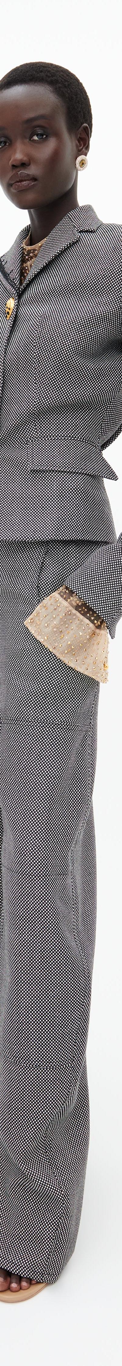 A woman wearing a grey Schiaparelli tailored jacket and wide-leg trousers with gold sculptural buttons