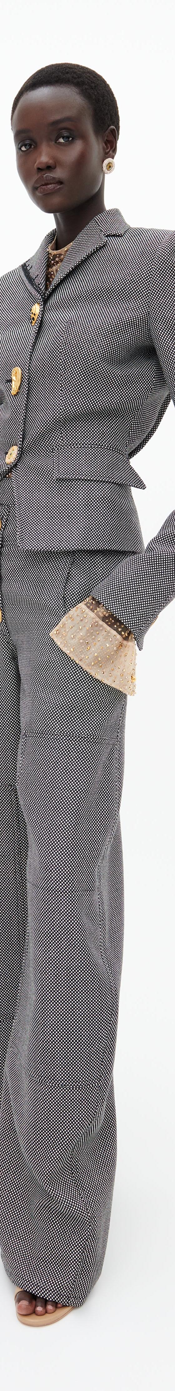 A woman wearing a grey Schiaparelli tailored jacket and wide-leg trousers with gold sculptural buttons