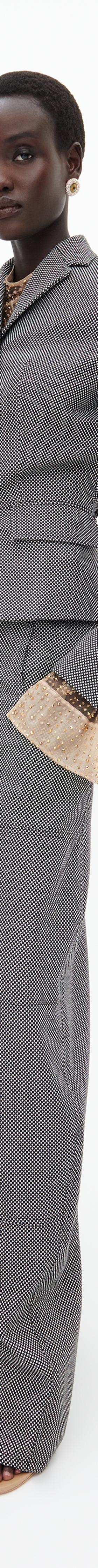 A woman wearing a grey Schiaparelli tailored jacket and wide-leg trousers with gold sculptural buttons