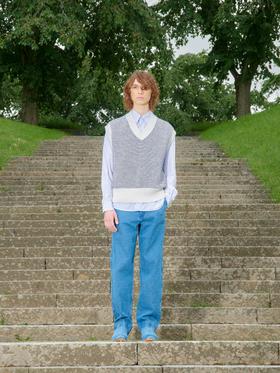 A man wearing a Schnayderman's knitted vest over a blue striped shirt with blue jeans