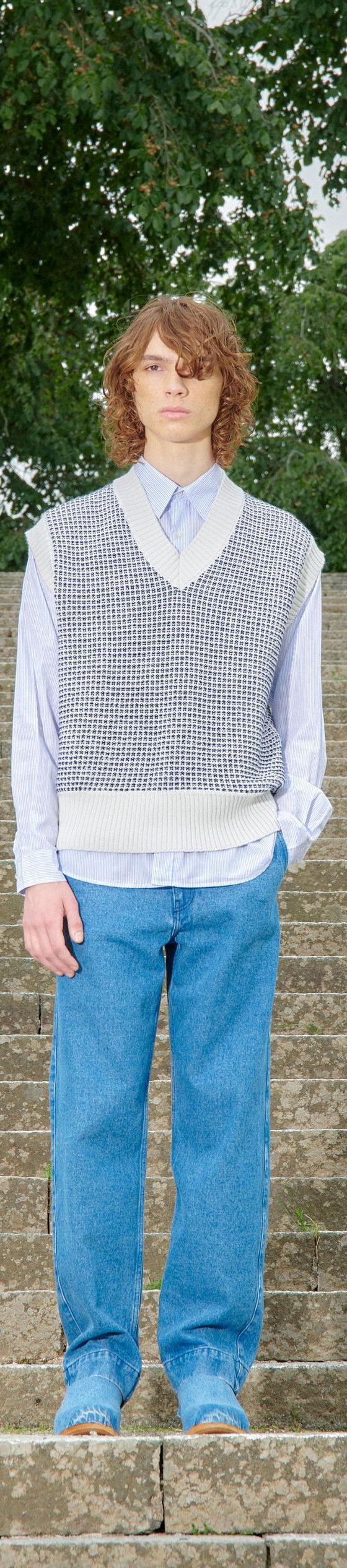 A man wearing a Schnayderman's knitted vest over a blue striped shirt with blue jeans