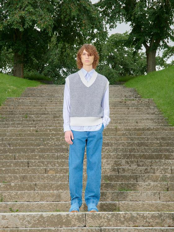A man wearing a Schnayderman's knitted vest over a blue striped shirt with blue jeans