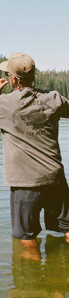 A man fly-fishing in a lake wearing a grey Seager Co. long sleeve tee and a snapback cap